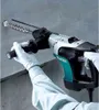 A person wearing white gloves is using a Makita rotary hammer drill to drill into a concrete wall. Produktbild-Vorschau