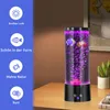 A lava lamp with fish is displayed on a wooden table, with decorative elements and text overlays on the left. Produktbild-Vorschau