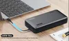 A black power bank is connected to a laptop with a blue charging cable, placed on a wooden desk. Produktbild-Vorschau