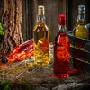 Several bottles of colored liquid are arranged on a rustic wooden surface with straw and wood elements. Produktbild-Vorschau