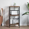 A narrow bookshelf with four shelves, decorated with a small plant and a framed picture, placed in a room next to a sofa and a large plant. Podgląd zdjęcia produktu