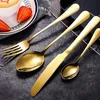 A set of gold cutlery is arranged on a dark surface, with a plate of strawberries and a cup of coffee in the background. Anteprima dell’immagine prodotto