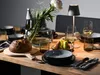 A table setting with a bread, fruit, wine glasses, and a vase of flowers. Produktbild-Vorschau
