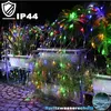 A string of colorful lights draped over plants at night, with a cobblestone path in the foreground. Voir les images du produit