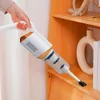 Weißer und oranger Handstaubsauger mit Bürstenaufsatz, von einer Hand gehalten, reinigt ein Holzregal Produktbild-Vorschau