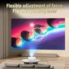 A projector is projecting an image onto a large screen in a living room setting. The projector is placed on a coffee table in front of a sofa. The image on the screen is abstract and colorful, with a circular graphic overlay indicating 'FOCUS'. Text at the Produktbild-Vorschau