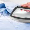 A person's hand is holding an iron and pressing it onto a blue shirt. Voir les images du produit
