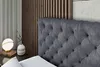 A close-up view of a tufted headboard of a bed, with a bedside table featuring a lamp and a vase. Produktbild-Vorschau