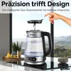 A glass electric kettle is shown on a countertop with a scenic mountain view in the background. A hand is shown removing the lid. Náhľad obrázku produktu