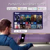 A man is holding a smartphone and looking at a smart TV displaying various streaming service logos. The TV is mounted above a purple cabinet. Náhľad obrázku produktu