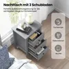 A grey nightstand with three drawers is shown next to a bed, with a window in the background. Icons and text highlight storage possibilities. Podgląd zdjęcia produktu