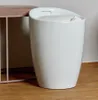 A white cylindrical stool with a padded seat sits on a wooden floor next to a pink stool. Produktbild-Vorschau