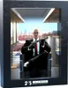 A framed image of Agent 47 sitting in a chair holding a gun, with a city skyline in the background. The frame has a "25 HITMAN ANNIVERSARY" logo at the bottom. Podgląd zdjęcia produktu