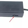 A close-up view of a black power adapter with a red arrow pointing to a small switch. Produktbild-Vorschau