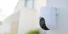 A white dome security camera is mounted on a white wall, with a blurred house and greenery in the background. Anteprima dell’immagine prodotto