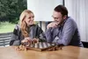 A couple playing chess at a table indoors, with a view of greenery outside. Podgląd zdjęcia produktu