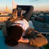 A person is lying on a rooftop, holding a smartphone, with a city skyline in the background during sunset. Anteprima dell’immagine prodotto