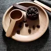 Two wooden coffee scoops and coffee beans on a wooden plate, set on a textured gray surface. Anteprima dell’immagine prodotto