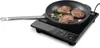A black induction cooker with a frying pan containing three pieces of meat, rosemary, and garlic. Náhled obrázku produktu