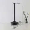 A black LED table lamp with dimensions indicated by text overlays, placed on a white surface next to a diffuser with reeds and flowers. Produktbild-Vorschau