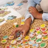 A child's hand is reaching for colorful wooden game pieces on a woven mat, with puzzle pieces scattered in the background. Anteprima dell’immagine prodotto