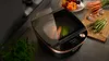 A modern kitchen appliance sits on a countertop, with fresh vegetables like carrots and asparagus nearby, suggesting healthy cooking. Produktbild-Vorschau