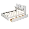 A white upholstered bed frame with wooden slats and two pull-out drawers is shown from a slightly elevated, diagonal angle against a white background. The headboard has built-in compartments and LED lighting. Náhľad obrázku produktu