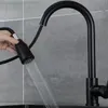 A hand is holding a black kitchen faucet spray head, with water spraying out, in front of a tiled wall. Produktbild-Vorschau