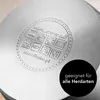 The bottom of a metal pot with embossed symbols and text, and a black circle with text overlay. Náhled obrázku produktu