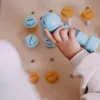 A child's hand is holding a toy drill, interacting with toy screws and bolts on a wooden surface. Produktbild-Vorschau