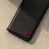 A close-up shot of a black leather phone case with red stitching and a red bull logo. Produktbild-Vorschau