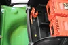 A close-up view of the battery compartment of a green lawnmower, showing two orange batteries and an orange tie-down strap. Produktbild-Vorschau