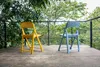 Two folding chairs on a concrete patio with a lush green background. Produktbild-Vorschau