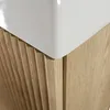 A close-up view of the corner of a white sink sitting on a wooden cabinet with a fluted front. Náhled obrázku produktu