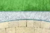 A close-up view of a garden border, showing artificial grass, white gravel, and yellow paving stones. Podgląd zdjęcia produktu