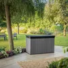 A garden storage box is placed on a patio in a garden setting, with trees and flowers in the background. Podgląd zdjęcia produktu