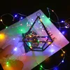A geometric glass terrarium with colorful LED string lights draped around it, placed on a book. Produktbild-Vorschau