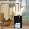 A black dehumidifier is shown in a room with a rocking chair and clothes hanging in the background. Produktbild-Vorschau