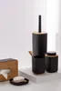 A collection of black bathroom accessories with wooden accents, including a tissue box, soap dish, toothbrush holder, soap dispenser, and toilet brush holder, arranged on a white surface against a white and light gray background. Náhled obrázku produktu