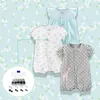 A collection of baby rompers and a box of snaps on a floral background. Produktbild-Vorschau