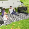A family is having a picnic on a patterned mat next to a camper trailer. Produktbild-Vorschau