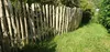 A wooden picket fence runs along a grassy path, with lush green foliage in the background. Produktbild-Vorschau