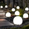 Several illuminated spherical garden lights are arranged in a garden setting at night, with a stone pathway leading up to them. Produktbild-Vorschau