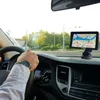 A person's hand is on the steering wheel of a car, with a GPS device mounted on the dashboard. Náhled obrázku produktu