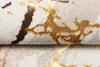 A close-up view of a textured rug with a marble-like pattern in beige, gold, brown, and rose gold. Voir les images du produit
