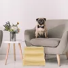 A pug wearing a bow tie sits on a gray armchair next to a side table with a vase of flowers. A yellow dog stair is in the foreground. Náhled obrázku produktu