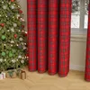 A Christmas tree decorated with ornaments and lights, next to red plaid curtains and gift boxes on a wooden floor. Produktbild-Vorschau