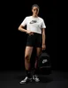 A woman is posing in front of a black background, wearing Nike apparel and holding a Nike backpack. Produktbild-Vorschau