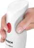 A hand is holding a white Bosch Clever Mixx hand blender, pressing the red power button. Náhľad obrázku produktu