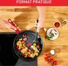 A person is cooking vegetables and chicken in a pan on a stovetop, with various ingredients like chili peppers, garlic, and spices arranged around the pan. Anteprima dell’immagine prodotto
